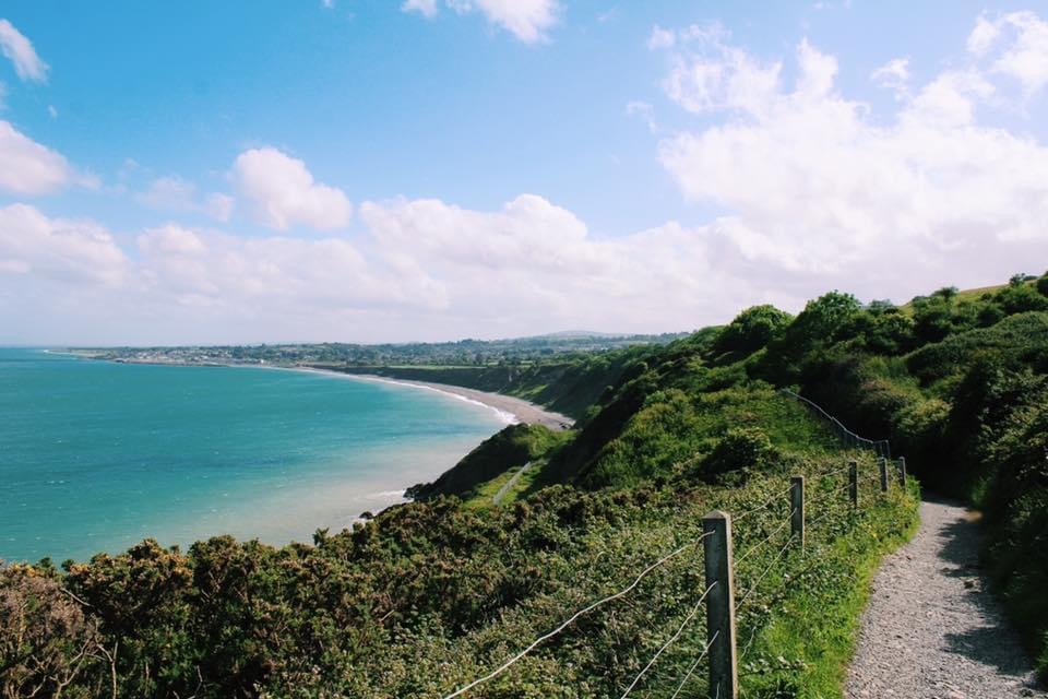 A scenic coastal walking path with views of the turquoise sea and rolling green hills along the Bray to Greystones Cliff Walk in Ireland.