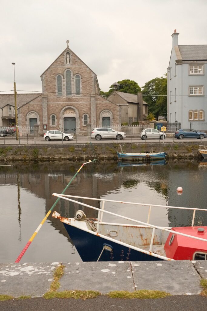 View of a serene canal with a small boat and a historic church in Galway City, showcasing the city's blend of cultural heritage and scenic charm, ideal for a 1-day itinerary.