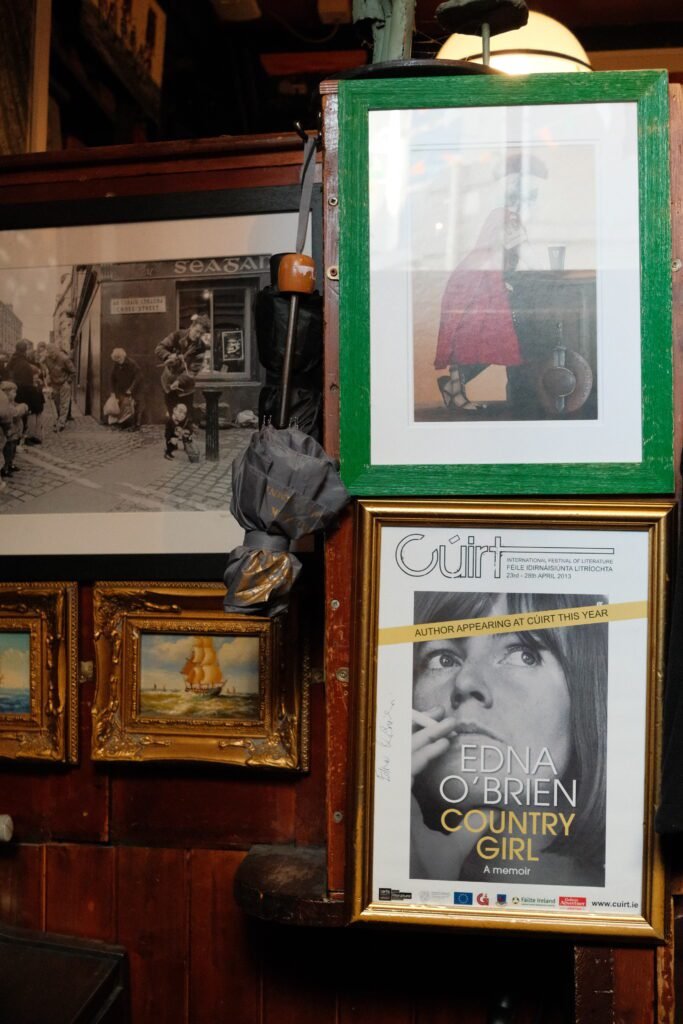 Interior of a historic Galway pub featuring framed artwork, vintage photos, and a poster for Edna O'Brien’s memoir, 'Country Girl.' The decor reflects the rich cultural and literary history often found in Galway’s most famous and historic pubs.