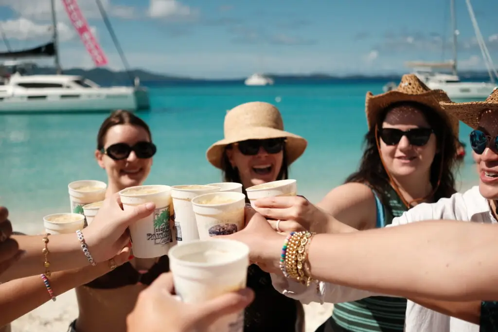 A group of friends toasting with Painkiller cocktails on the beach at the Soggy Dollar Bar during a girls' bachelorette trip from St. Thomas to the British Virgin Islands.