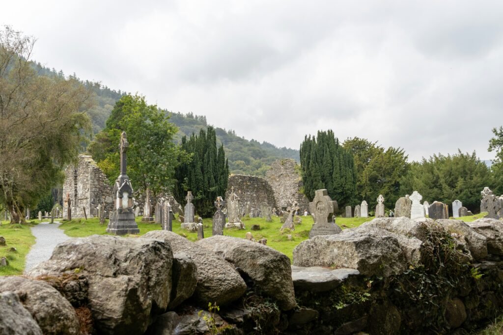 Ancient cemetery with Celtic crosses and ruins at Glendalough Monastery in Ireland, surrounded by green hills and trees.