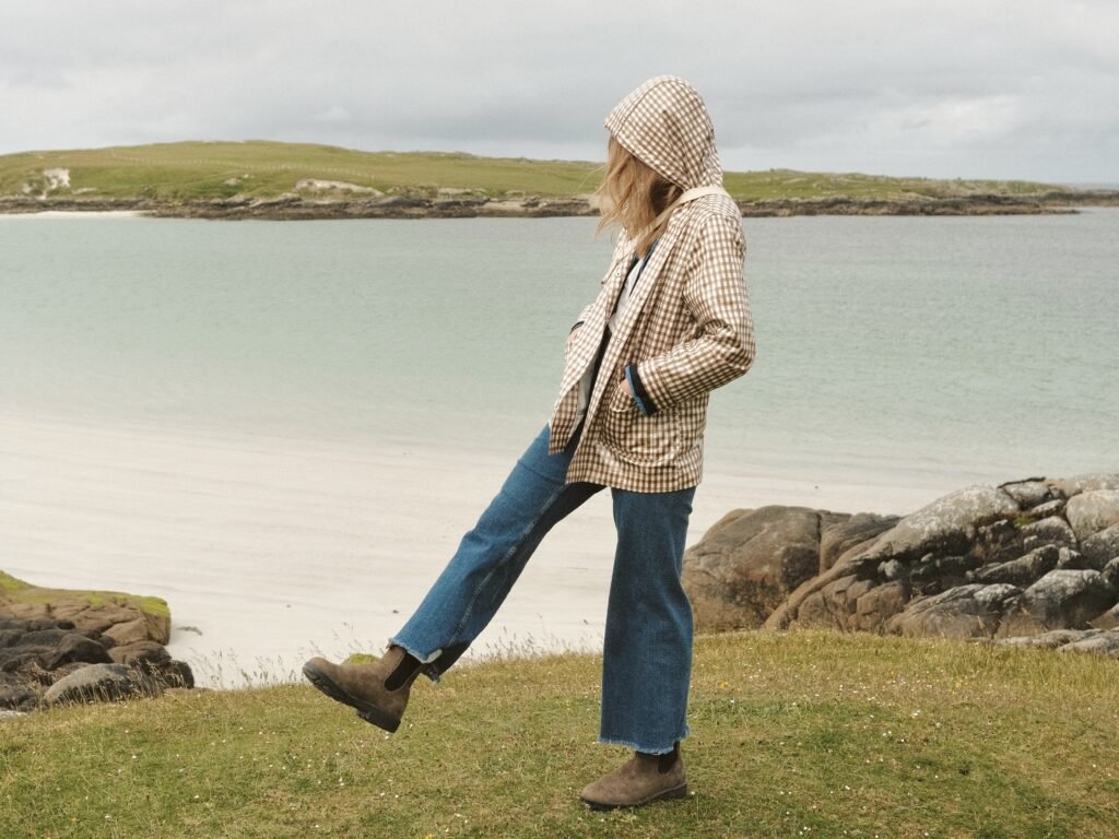 Traveler wearing a checkered rain jacket and boots, walking along a scenic beach in Ireland. Perfect visual for packing tips on how to stay warm and dry while exploring Ireland’s coastal regions and unpredictable weather. Features stylish yet practical travel clothing for an outdoor Irish adventure.