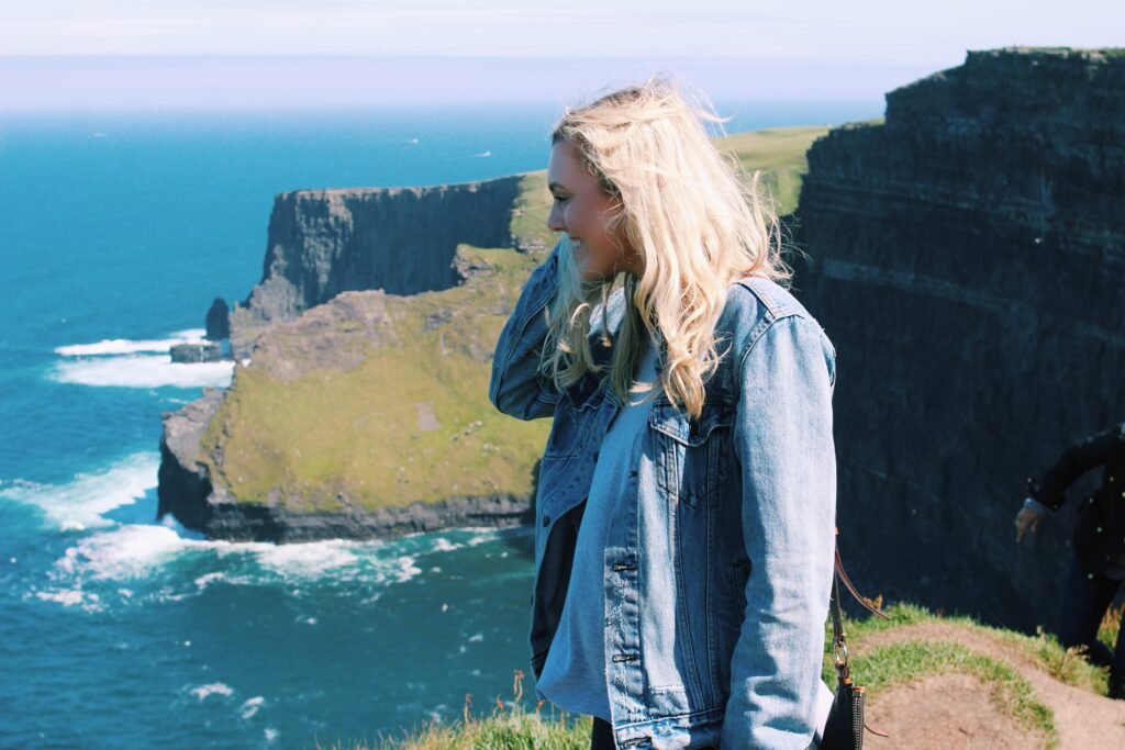 Kaley smiling at the Cliffs of Moher in Ireland, with dramatic cliffs and the Atlantic Ocean in the background.