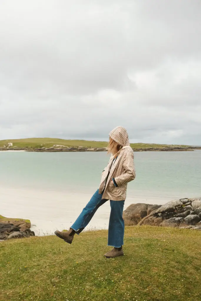 Kaley, travel blogger from Kindred Compass, standing on a beach in Connemara, County Galway, Ireland, with her foot playfully raised and the serene waters in the background.