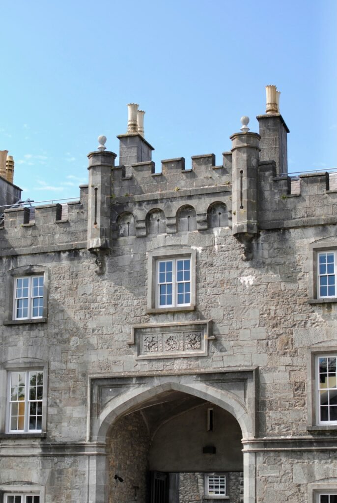 A close-up of a medieval stone archway at Kilkenny Castle, featuring intricate carvings and towers with decorative chimneys.