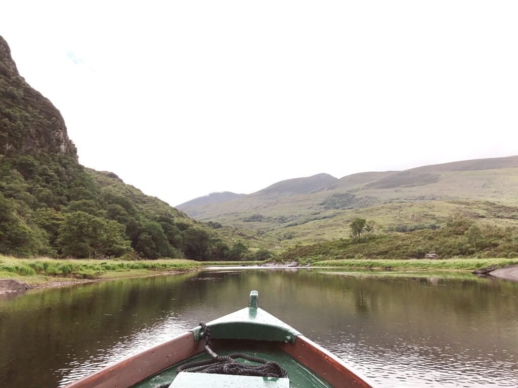 A scenic boat ride from the Gap of Dunloe across the lakes of Killarney National Park, with calm waters reflecting the green mountains of the Irish countryside.