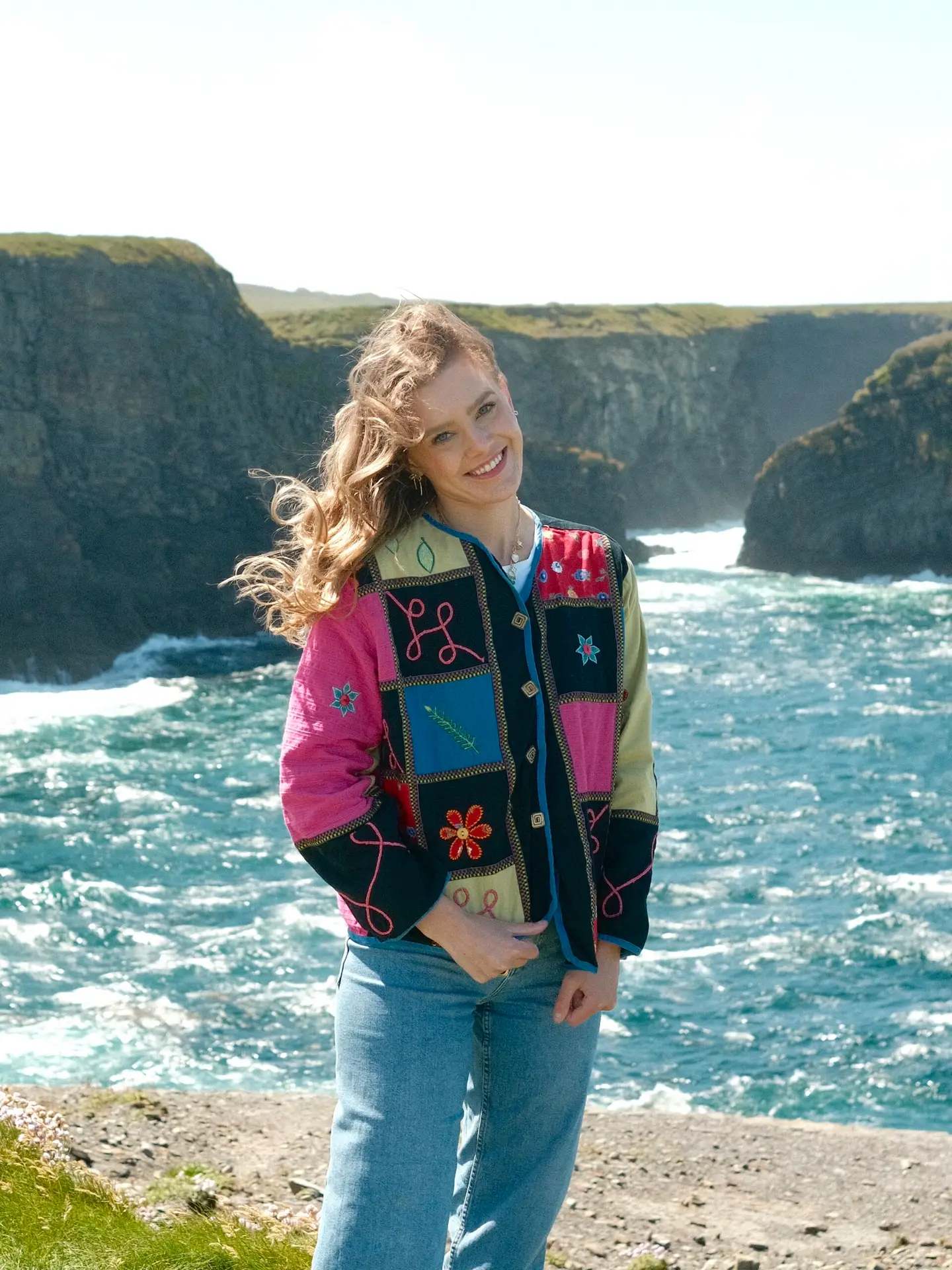 Kaley, travel blogger from Kindred Compass, standing by the scenic cliffs on the coast of Ireland, smiling with the ocean in the background.