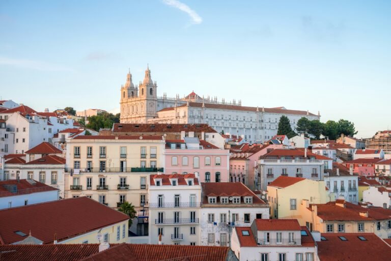 View of the historic Alfama district in Lisbon with pastel-colored buildings and the Church of São Vicente de Fora in the background.