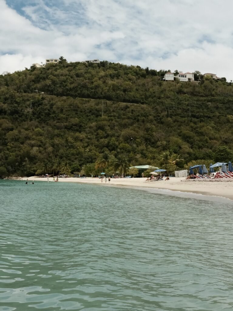 A scenic view of the shoreline and hills at Magens Bay Beach, St. Thomas, with beach chairs and umbrellas lining the sand.