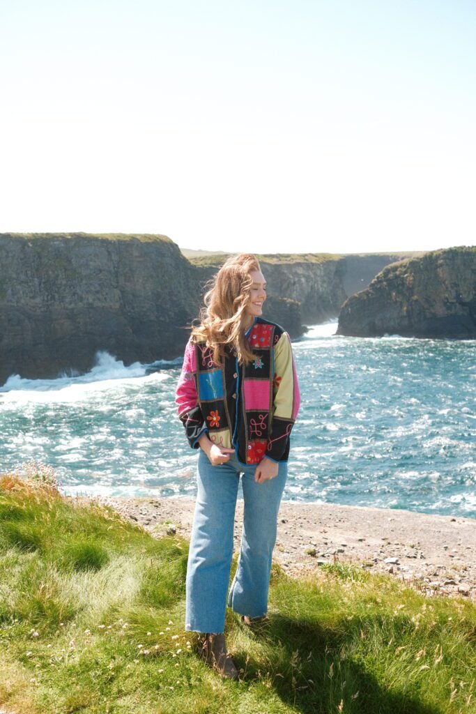 Standing on the grassy edge of the Kilkee Cliffs in County Clare, Ireland, with the stunning cliffs and crashing waves of the Atlantic Ocean as a dramatic backdrop. The natural beauty of this coastal landscape shines through in this vibrant moment, making it truly one of the best cliffs in Ireland to visit.