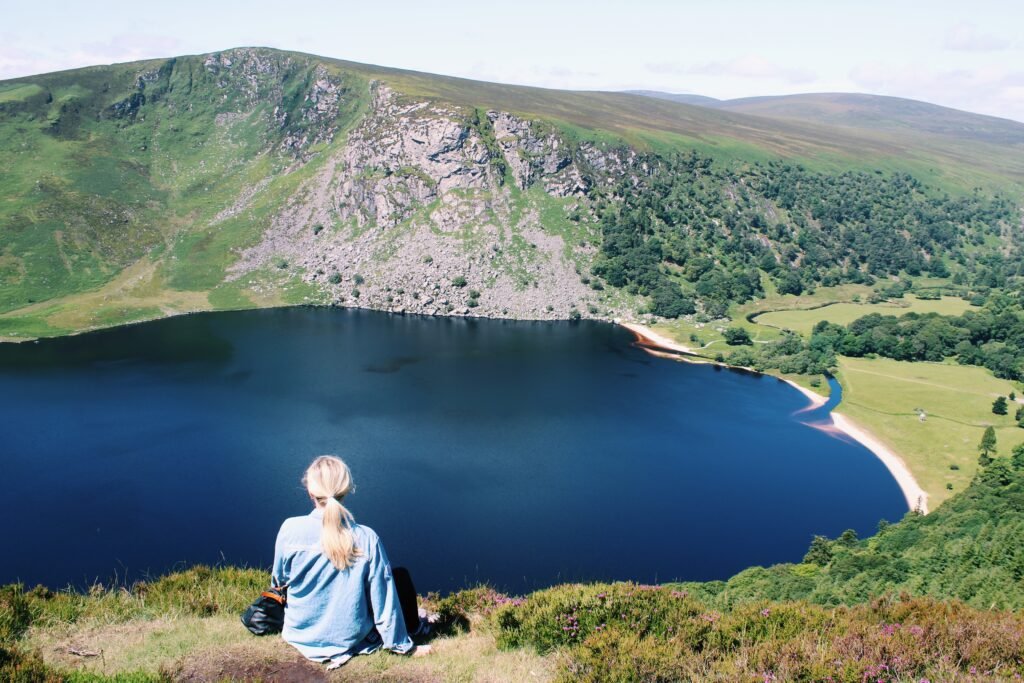 Sitting on a hilltop overlooking a serene lake surrounded by green mountains in Wicklow, Ireland, one of the most popular day trips to take from Dublin.