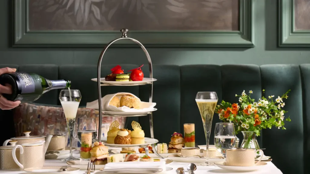 This image shows an elegant afternoon tea setup at Killarney Park Hotel, featuring a beautifully set table with tiered trays of scones, pastries, and finger sandwiches. Champagne is being poured into glasses, adding a luxurious touch to the experience. The table is adorned with fine china and a small vase of fresh flowers, creating a sophisticated and inviting atmosphere. This scene captures the essence of afternoon tea in Killarney, where guests can indulge in a refined culinary experience in a beautifully designed setting.