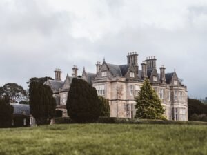 Exterior view of Muckross House in Killarney, Ireland, surrounded by lush green lawns and manicured trees. This 19th-century mansion, located in Killarney National Park, is a popular attraction for visitors exploring County Kerry and looking to experience Irish history and natural beauty.